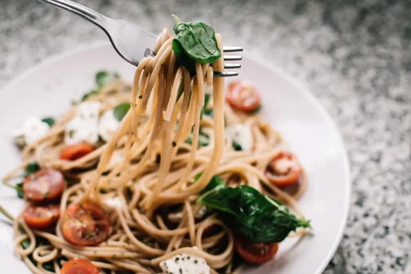 Massa com folhas verdes, tomates e queijo em um prato de cerâmica.