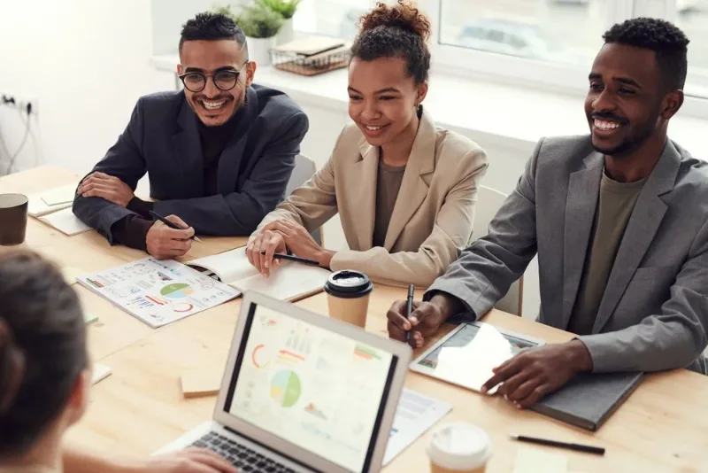 Equipe em reunião de trabalho, com cadernos, gráficos e notebook.
